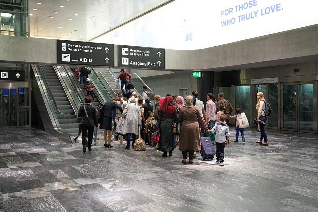 Women in headscarves, children and men stand at an escalator at Zurich airport.